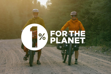 Two cyclists standing with loaded touring bikes on a forest gravel road during golden hour light