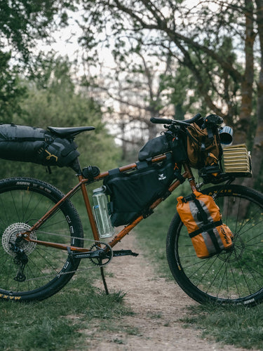 Adventure touring bicycle fully loaded with bikepacking bags on forest trail surrounded by green trees