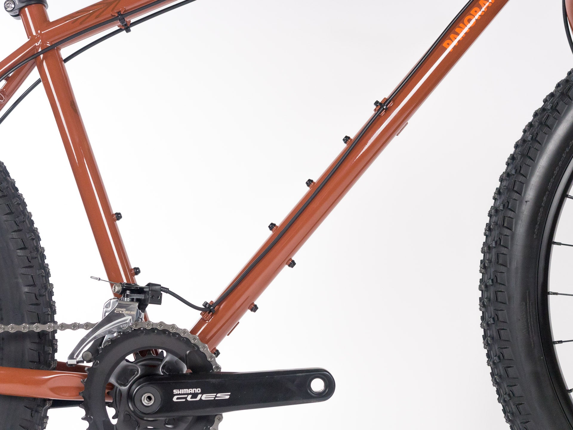 Close-up of brown bike frame with Shimano crankset and knobby tires on a white background