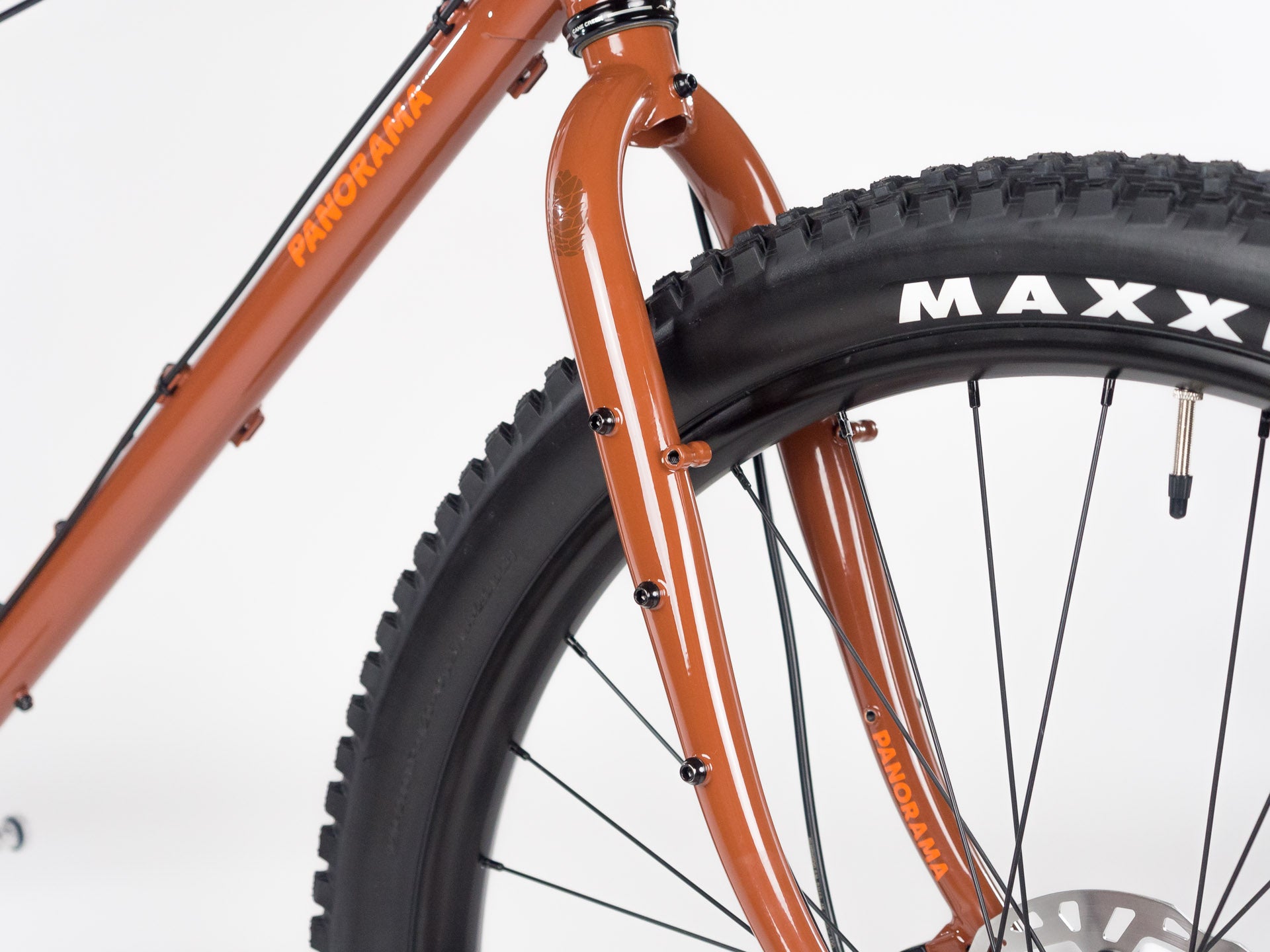 Close-up of rust-colored Panorama Cycles touring bike front fork with disc brake mount and knobby Maxxis tire on white background