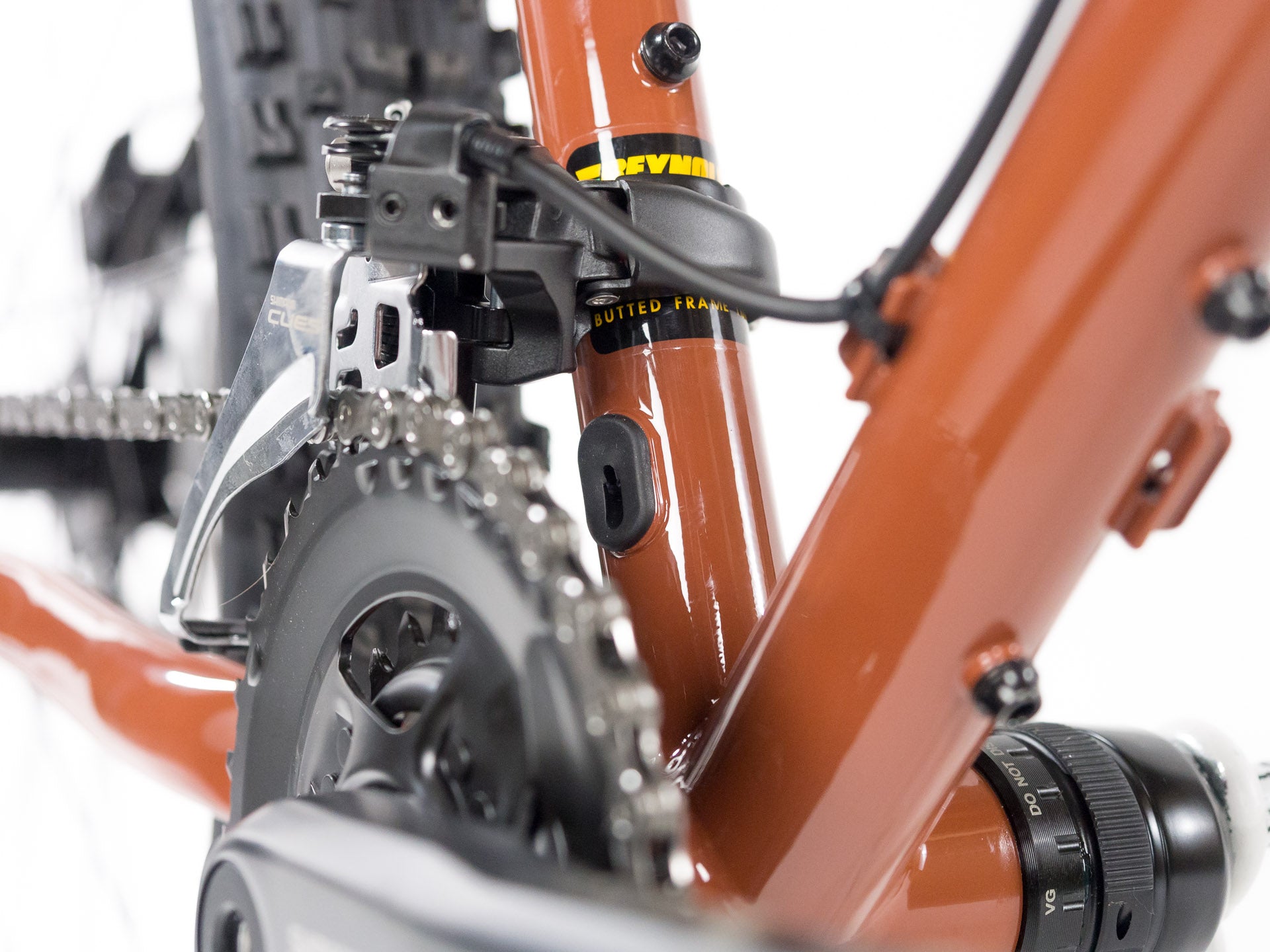 Close-up of rust-colored bicycle frame showing drivetrain, front derailleur, and chainring with detailed components on white background