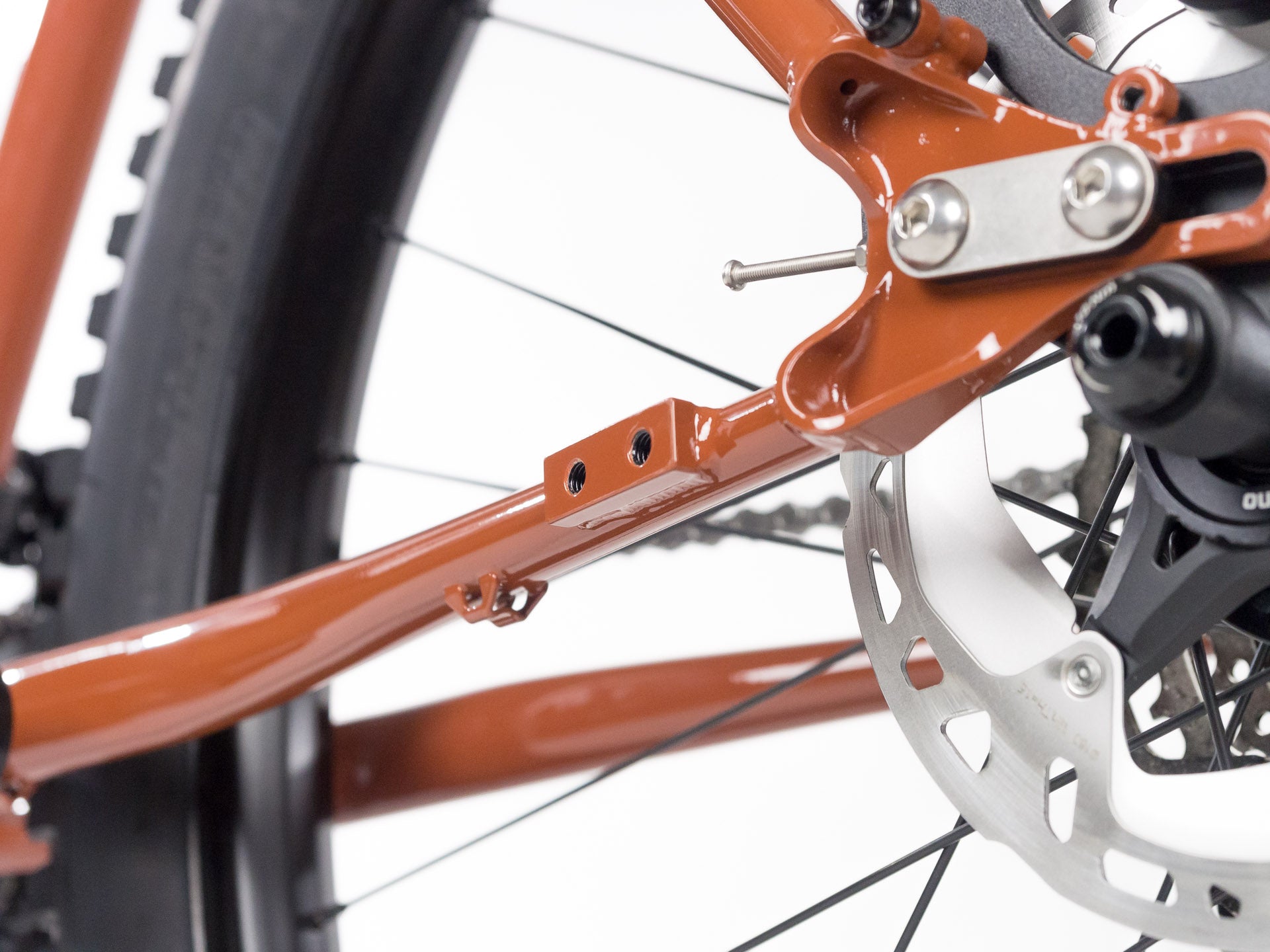Close-up of rust-colored bicycle frame rear triangle with disc brake rotor and wheel spokes on white background