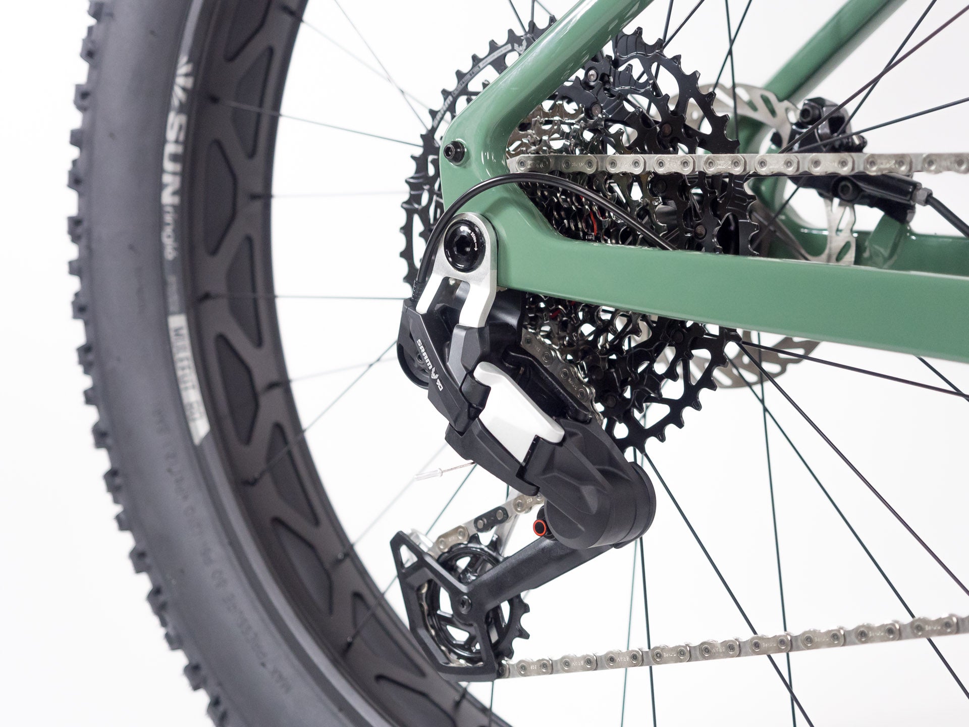Close-up of green bicycle rear derailleur, cassette, chain, and fat tire on white background