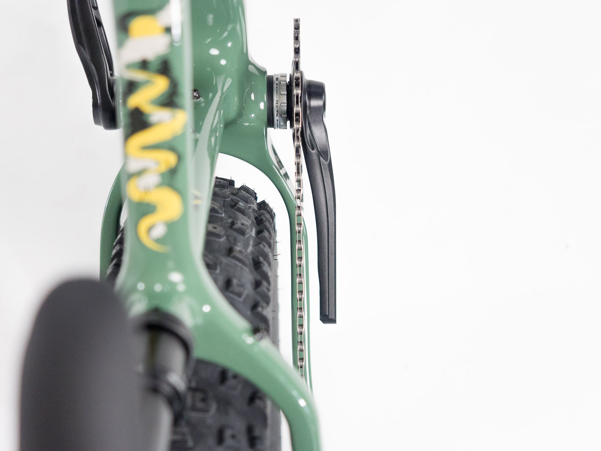 Close-up of green bicycle frame showing chainstay, knobby tire, and crank arm on plain white background