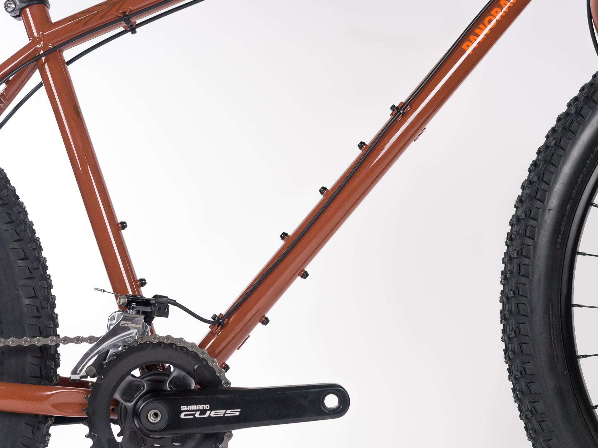 Close-up of brown touring bike frame with Shimano crankset and knobby tires on white background