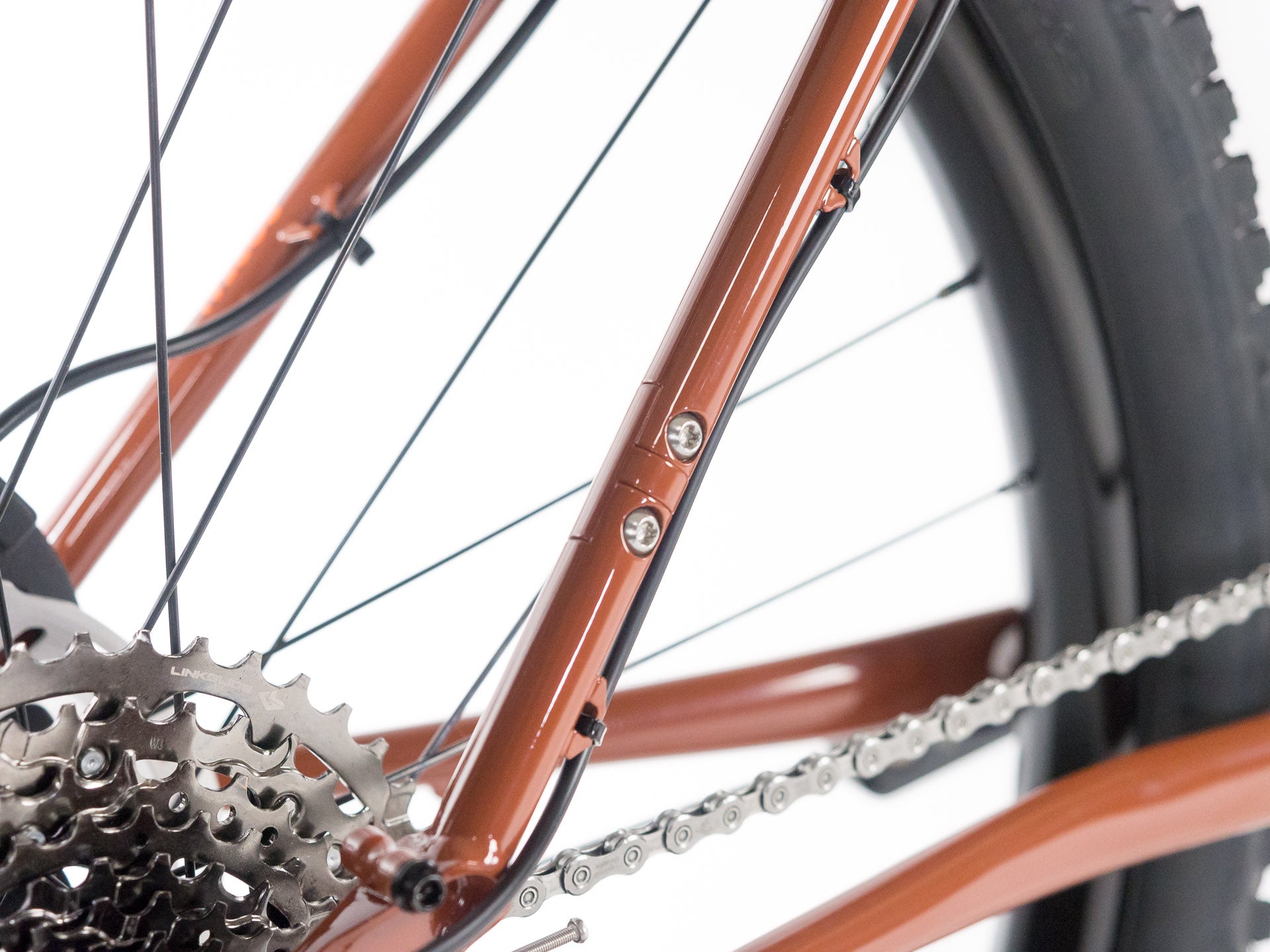 Close-up of rust-colored bicycle frame showcasing rear dropout, gear cassette, chain, and part of tire with tread details