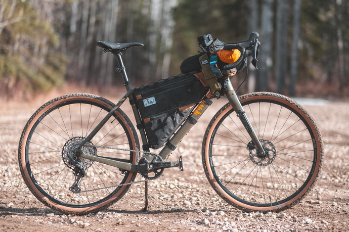 Gravel bike with bikepacking bags attached to frame and handlebars on a dirt trail in forest setting